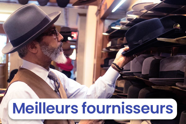 Homme au Borsalino recherchant un chapeau sur un étalage avec marqué Meilleurs fournisseurs
