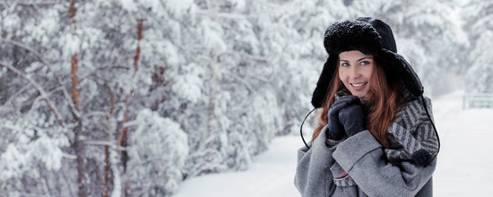 Femme souriante portant une chapka noire et un manteau gris dans la neige